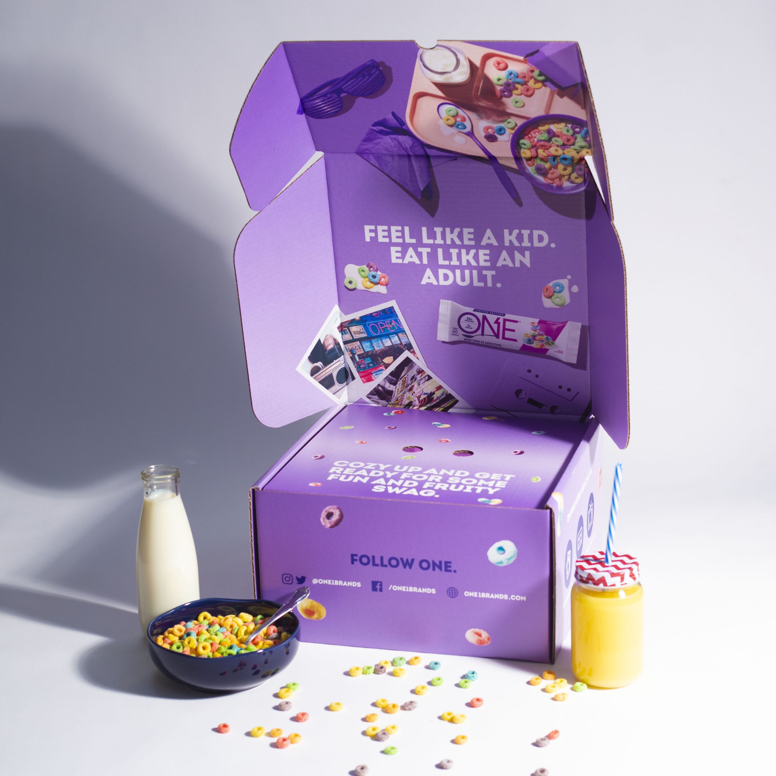 purple branded "One" box with brightly colored circled cereal on it and milk and a bowl of cereal next to it